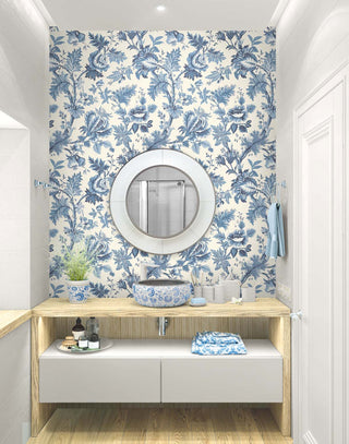 Elegant bathroom with blue & cream Toile de Jouy wallpaper. Features a round white mirror, light-wood counter, patterned blue ceramic vessel sink, and floating white cabinet.