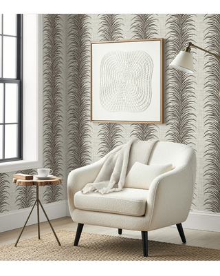 A styled interior corner showing a cream boucle armchair with a throw pillow and blanket, a small round wooden side table with a cup, patterned wallpaper with a repeating palm leaf design, a framed abstract print on the wall, and a floor lamp.