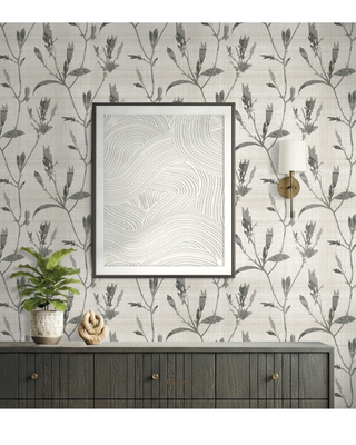 A styled interior scene showing a framed abstract art print hanging on a wall with botanical wallpaper, a wall sconce, a dark wood console table, and a potted plant.