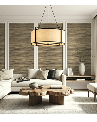 A modern living room featuring a large cylindrical pendant light with a beige fabric shade and black metal frame hanging above a white sofa. The background consists of vertical wood slat wall panels framed in white, with a rustic wood slab coffee table and a white vase in the background.