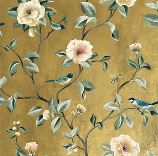 Close-up swatch of Crown's Chinoiserie collection wallpaper in the Arang Floral Trail pattern. The striking design features a textured, gold background with a subtle, painterly finish. Elegant, branching trails climb across the canvas, bearing large, beautifully rendered camellia-like blossoms in shades of soft cream, pale yellow, and delicate blush pink. Sage green leaves with prominent highlights and several small, detailed songbirds perched on the stems complete the dramatic botanical aesthetic
