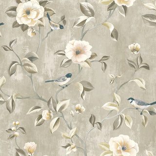 Close-up swatch of Crown's Chinoiserie collection wallpaper in the Arang Floral Trail pattern. The striking design features a textured, soft grey background with a subtle, painterly finish. Elegant, branching trails climb across the canvas, bearing large, beautifully rendered camellia-like blossoms in shades of soft cream, pale yellow, and delicate blush pink. Sage green leaves with prominent highlights and several small, detailed songbirds perched on the stems complete the dramatic botanical aesthetic