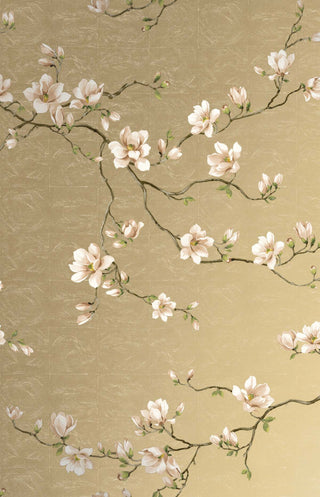 Close-up swatch of Crown's Chinoiserie collection wallpaper in the Moonlace Magnolia pattern. The elegant design features a shimmering, metallic gold background with a faint, block-grid texture overlaid by subtle, swirling line details. Graceful, dark brown branches twist across the canvas, bearing large, delicate white magnolia blossoms with soft pink undertones and small green leaves and buds. The botanical motif offers a luxurious, serene, and sophisticated aesthetic